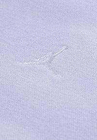 Lyseblåt stof med et broderet hvidt Jumpman-logo. Teksturen er glat med en fin, ensartet vævning.