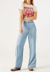 Jeans de denim de pierna ancha en un tono azul claro con cintura alta, combinados con una camiseta gráfica que presenta diseños multicolores.