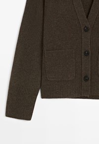 Bruine gebreide cardi met een v-hals, ribbelstructuur, vier zwarte knopen en een voorzak. Zacht materiaal, casual ontwerp.