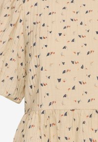Katoenen jurk in off-white met een gestructureerde afwerking, voorzien van een morekleurig abstract patroon in tinten blauw, oranje en marineblauw.