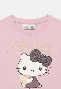 Roza dukserica s glitterastim "Hello Kitty" dizajnom, s točkastom mašnom i grafikom srca. Mekani materijal s okruglim izrezom.