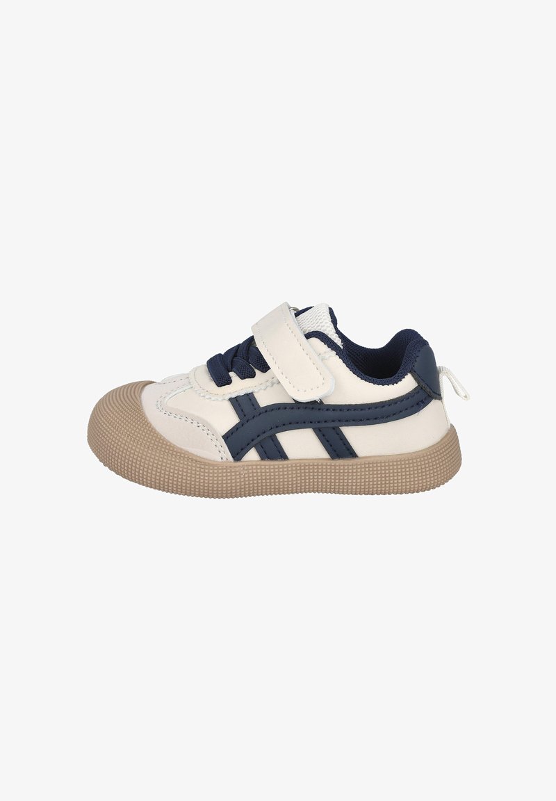 Zapatilla blanca y marina con una correa de velcro, suela texturizada beige y diseño lateral en capas con franjas oscuras marinas sobre una superficie lisa.