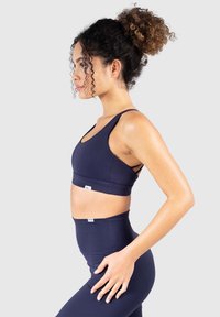 Sujetador deportivo azul marino y leggings de cintura alta hechos de tela elástica, con una textura suave y detalles de corte en las tiras del sujetador.