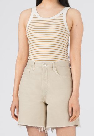 Osoba nosząca beżowe dżinsowe szorty z wysokim stanem i postrzępionymi krawędziami oraz biały top na ramiączkach z cienkimi poziomymi musztardowymi paskami.