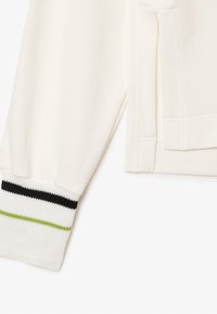 Manica di felpa bianca con polsino elasticizzato, caratterizzata da strisce nere, verdi e bianche. Texture morbida con dettagli di cucitura lungo la cucitura.