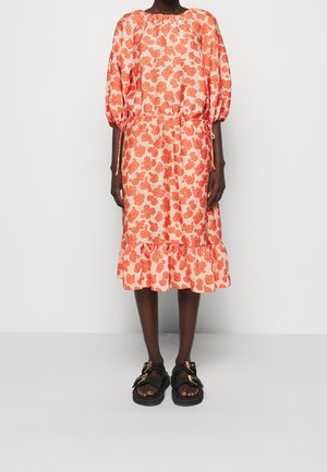 Blomklänning med orange blommor på en ljus bakgrund, insvängd midja, puffärmar och volangkant; matchas med svarta sandaler.