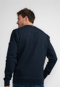 Marineblauw sweatshirt met ronde hals, ribgebreide manchetten en zoom; voorzien van een achterzak en een subtiel logo-detail bij de hals.