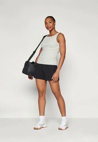 Pelēks bez piedurknēm tops, melnas šorti un balti sporta apavi. Modelis tur melnu somu. Gluda faktūra, ikdienas piegriezums, minimālisma dizains.