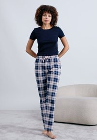 Camiseta de algodão azul-marinho combinada com calças de pijama de algodão xadrez que apresentam quadrados azul-marinho e rosa claro, com um cordão na cintura.