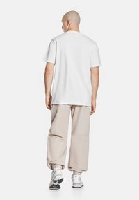 Biały bawe�łniany T-shirt o casualowym kroju. W połączeniu z beżowymi, luźnymi spodniami z elastycznymi mankietami. Białe buty sportowe z czarnymi podeszwami.