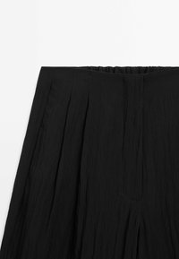 Pantalon noir plissé avec une taille élastique, fabriqué dans un tissu léger et texturé. Présente un design épuré sans aucune fermeture visible.