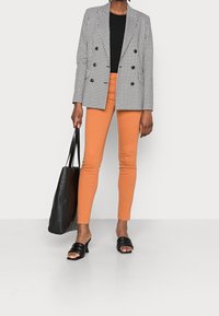 Blazer de cuadro houndstooth en blanco y negro, top negro, pantalones skinny naranjas, bolso de mano negro, sandalias negras con tiras.