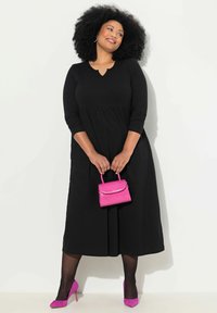 Robe noire à manches longues avec un décolleté en forme de clé, une jupe évasée, associée à un petit sac à main en cuir crocodile rose et des talons en suédine rose.