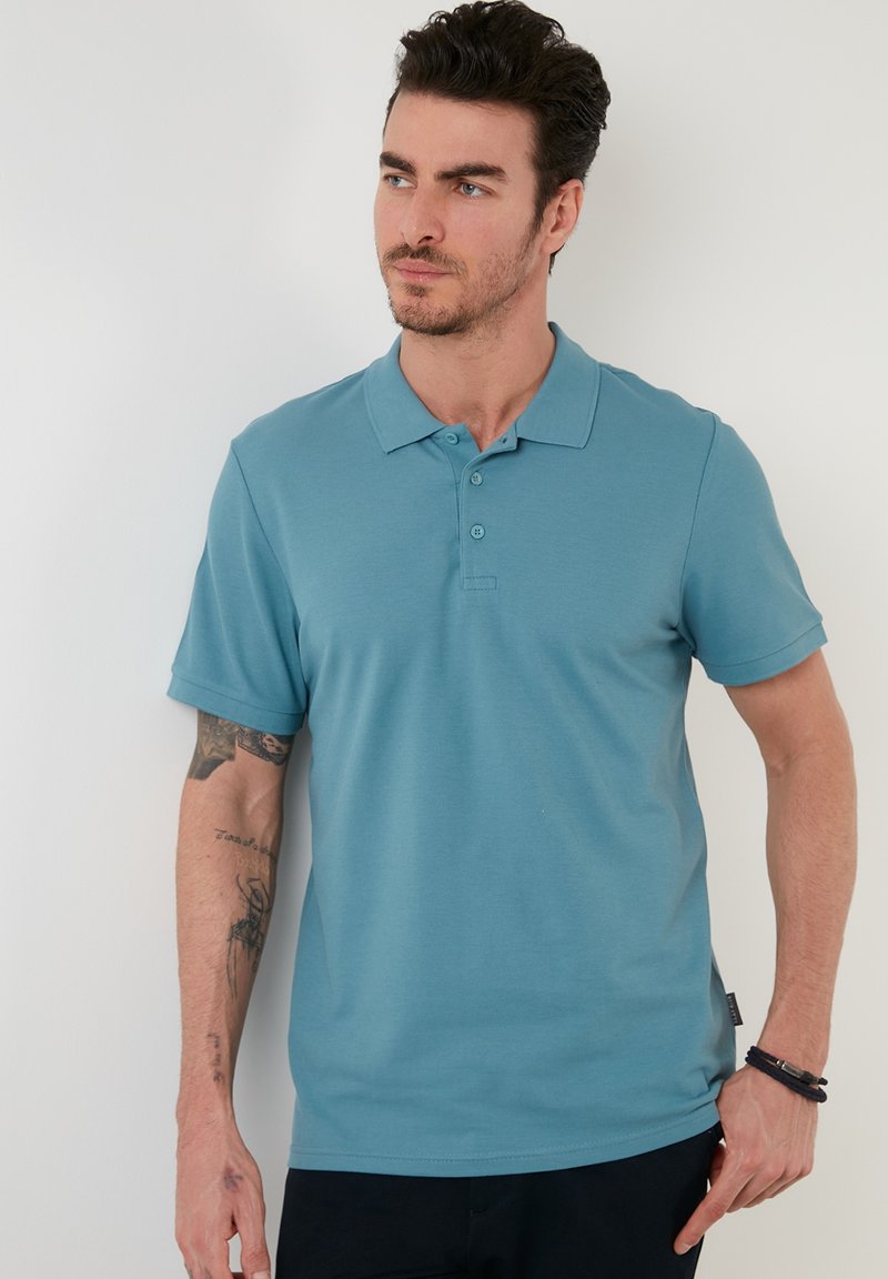 Polo shirt de culoare albastru deschis, fabricat dintr-un amestec de bumbac. Dispune de un guler cu nasturi, plachetă cu trei butoane și mâneci scurte cu o croială dreaptă.