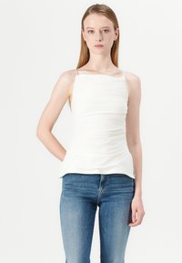 Witte, aangesloten camisole met dunne bandjes, geplooid materiaal bij het lijfje en een uitlopende zoom, gecombineerd met blauwe skinny jeans.