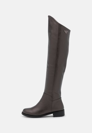 Stivale alto fino al ginocchio in pelle marrone scuro, tacco basso e punta arrotondata, con logo laterale vicino alla parte superiore.