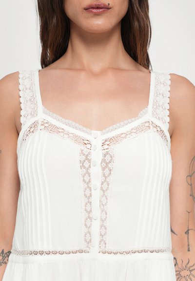 Vestido blanco con ribete de encaje y cierre de botones, que presenta rayas verticales y un corsé ajustado. Textura delicada y tirantes con forma de escallola.