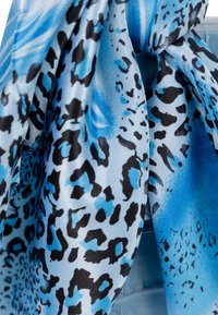 Tissu imprimé animal bleu et noir avec une texture fluide, présentant des taches irrégulières et des motifs abstraits sur un matériau soyeux.