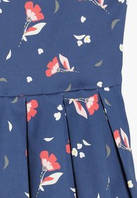 Květinové šaty z tmavě modré látky s červenými květy a menšími bílými akcenty, s nabráním a hladkou texturou.