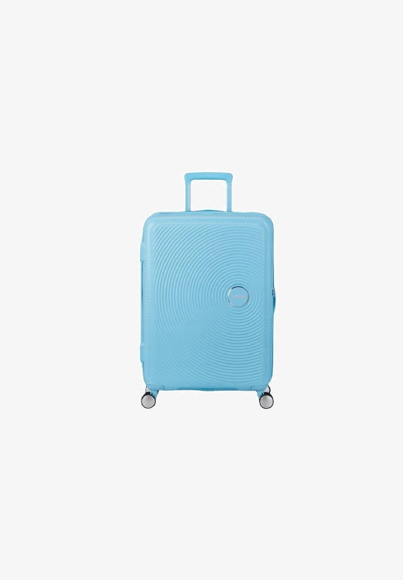 Valigia rigida azzurro chiaro con manico telescopico esteso, design a cerchi concentrici testurizzati e quattro ruote girevoli su sfondo bianco.