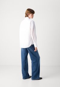 Hvit skjorte med lange ermer, buet kant, sammen med vide blå denimjeans. Glatt stoff med minimal detaljering.