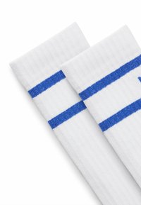 Valkoiset puuvillasukat, joissa on kaksi horisontaalista sinistä raitaa. Kangas on ribattua, ja varret on hieman rullattu.