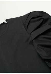 Vêtement noir avec un col rond et une manche bouffante volumineuse en tissu froncé sur un fond clair.
