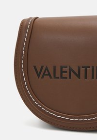 Borsa in pelle marrone con design arrotondato, logo "VALENTINI" embossato e dettagli di cucitura bianca. Texture liscia, stile minimalista.