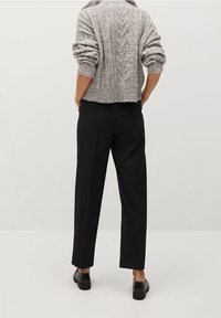 Šedý krátký svetr s copánkovým vzorem a ohrnutými rukávy, doplněný černými volnými kalhotami a černými botami, představující minimalistický styl.