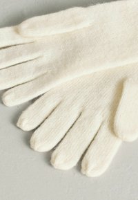 Krém színű kötött kesztyű, puha, texturált anyagból készült. Öt ujjal rendelkezik, lekerekített hegyekkel és varrás nélküli kivitelben.