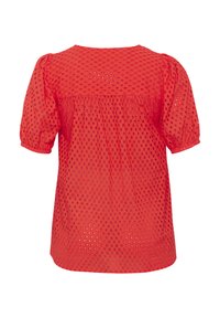 Haut rouge à manches courtes fabriqué en tissu texturé avec de petits motifs découpés, présentant un dos froncé et un col arrondi.