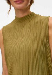 Olijfgroene mouwloze top met een hoge, geribbelde halslijn en verticale plooien, die de zachte textuur en vloeiende ontwerp benadrukt.