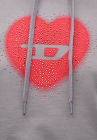 Šedá mikina s kapucňou, na ktorej je červený motív srdca ozdobený malými kamienkami. Šnúrky sú sivé a látka má hladkú textúru.