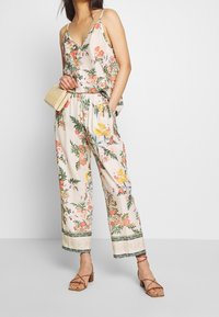 Giubbotto floreale con sfondo crema, spalline sottili e pantaloni larghi con rifiniture decorative e un motivo di fiori colorati.