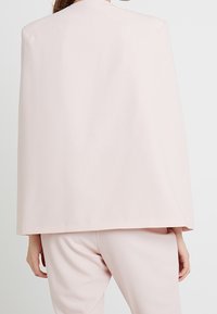 Vaaleanpunainen viittatyylinen päällysvaate, valmistettu sileästä kankaasta. Siinä on yksinkertainen siluetti ilman näkyviä kiinnityksiä tai koristuksia.