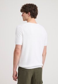 Maglione a maniche corte bianco in maglia con scollatura a girocollo. Presenta dettagli testurizzati sottili sulle spalle. Tessuto morbido, vestibilità rilassata.