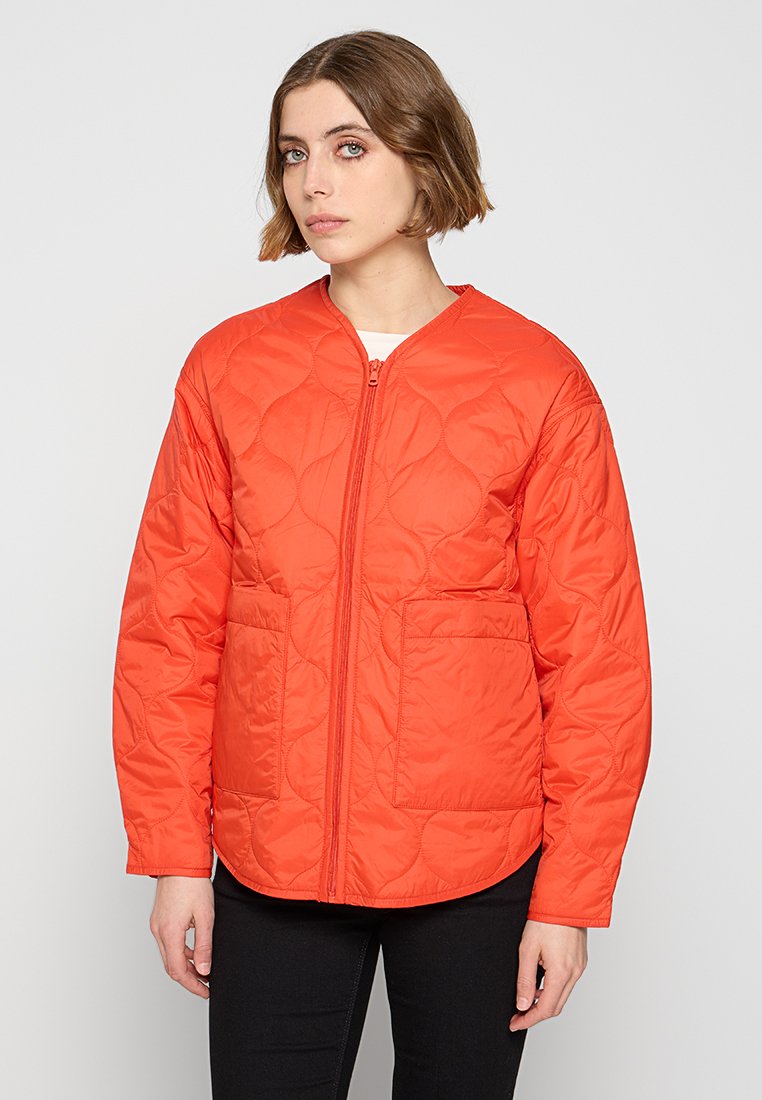 Kurtka z pikowanej tkaniny w kolorze pomarańczowym, z okrągłym dekoltem, zapięciem na zamek z przodu oraz dwiema dużymi kieszeniami, o gładkim, błyszczącym wykończeniu.