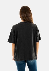Zwarte oversized t-shirt met korte mouwen, een ronde hals en een zachte textuur, gecombineerd met blauwe spijkerbroek.