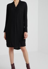 Vestido negro de manga larga con escote en V, de corte recto, con una longitud a mitad del muslo y un dobladillo ligeramente curvado. Textura de tela suave.