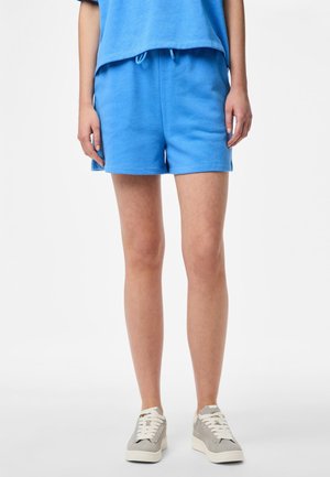 Shorts en coton bleu avec une taille élastique et un cordon de serrage. Fabriqués en tissu doux, avec des poches latérales et une coupe décontractée. Portés avec des baskets grises.