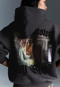 Sweatshirt à capuche gris foncé avec un grand imprimé graphique de deux figures, avec le texte "Que Dieu" et "Frankenstein" en police gothique noire.