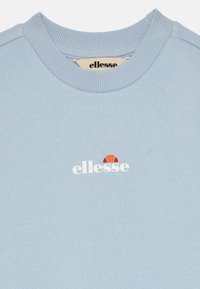 Gai zilgans džemperis, izgatavots no mīkstas auduma, ar ribotu apkakli un baltu "ellesse" logo, kā arī sarkanu akcentu virs teksta.