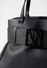 Borsa a tracolla in pelle nera con texture, dotata di una larga cintura e di una fibbia lucida nera con logo. Presenta manici corti e una forma strutturata.
