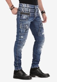 Schmale Jeans aus dunkelblauem Denim mit distressed Details, mehreren Fronttaschen und kontrastierendem weißen Nähten. Schwarzes Logo-Patch an der Taille.