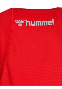Rød sportstrøje med mesh-struktur. Har et gråt "hummel" logo ved halsudskæringen og forstærket syning langs kanterne.
