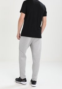 Grå bomullsbyxor med en avsmalnande passform, med detaljerade sidofickor, kombinerat med en svart T-shirt med kort ärm och svarta sneakers.