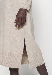 Abito in maglia beige con polsini e orlo a coste, caratterizzato da spacchi laterali. Tessuto morbido, design di lunghezza media. Aspetto minimalista senza motivi.
