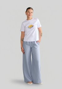 Biały t-shirt z krótkim rękawem z grafiką masła oraz niebieskie szerokie spodnie z lekkiego materiału, uzupełnione casualowymi sandałami.