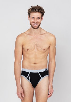 Schwarze Baumwollslips mit grauem elastischem Bund und Akzenten. Sie bieten eine enge Passform und ein minimalistisches Design. Das Modell steht mit neutralem Ausdruck.