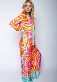 Buntes Zweiteiler-Outfit mit abstrakten Mustern in Orange, Pink und Türkis. Der Stoff hat eine glatte Textur, einen lockeren Sitz und lange Ärmel.